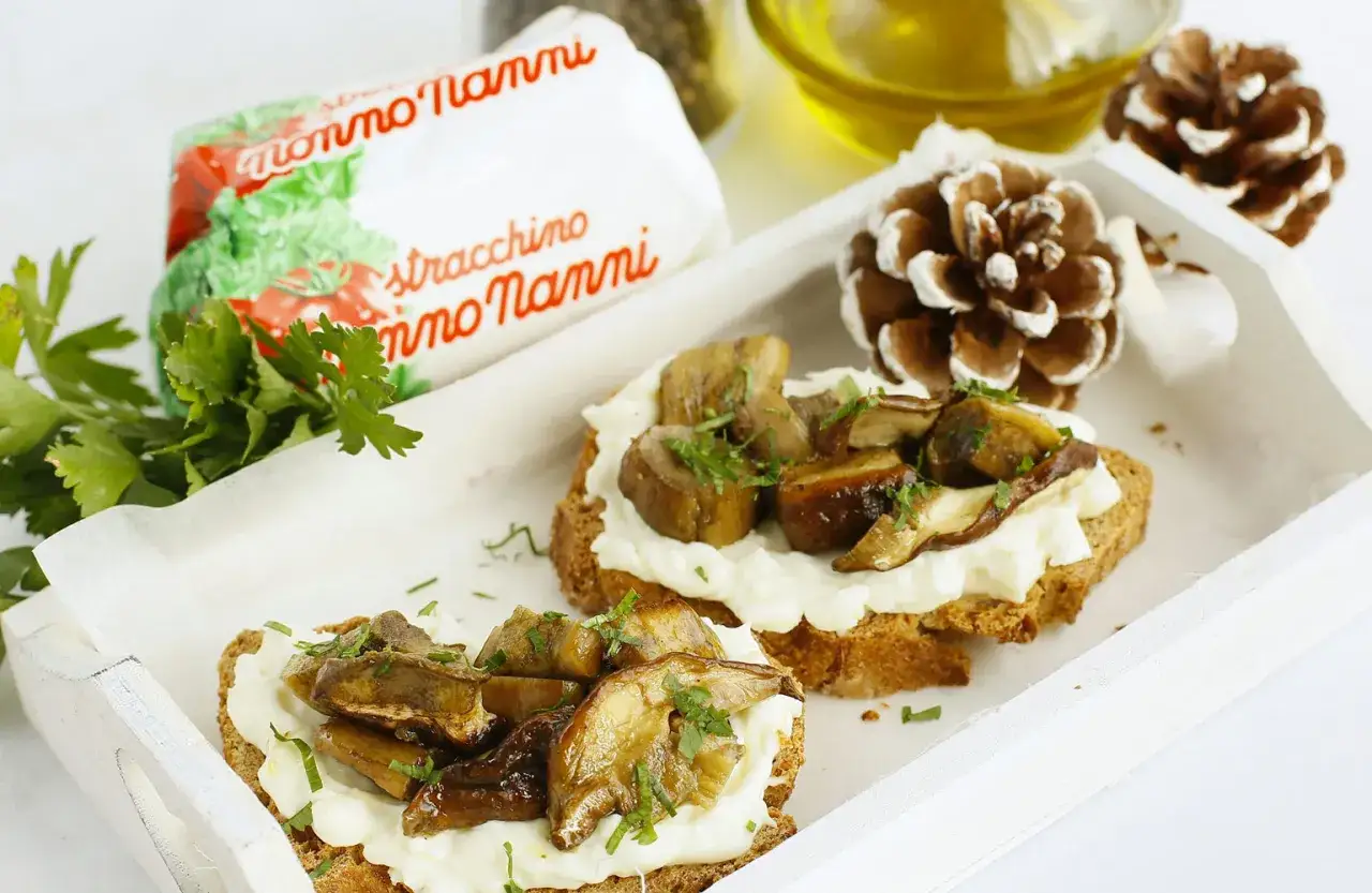 Bruschette con fonduta di stracchino e funghi trifolati, guarnite con prezzemolo fresco.