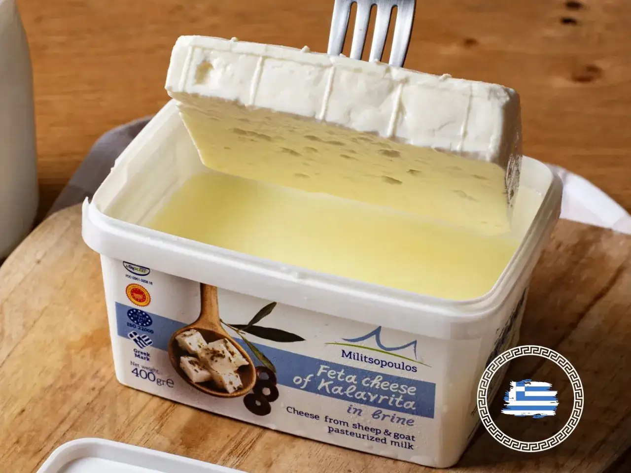 Un blocco di feta, formaggio greco, viene sollevato da una confezione in salamoia con una forchetta.