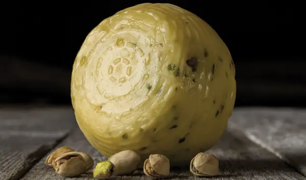 Formaggio pecorino al pistacchio, con alcuni pistacchi sparsi sul tavolo di legno.